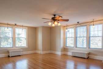 an empty living room with an overhead ceilng fan whose lights are lit