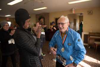 two women cheer an older man with a medal around his neck