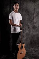 young man standing behind and holding his guitar upright