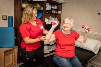 a physical therapist working with an elderly woman on lifting weights