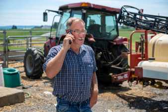 a farmer talking on his cell-phone standing in front of a tractor