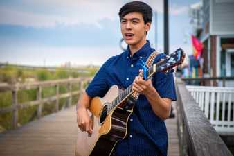 young man playing guitar on a boardwalk