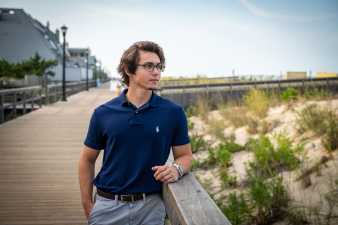 young man with glasses standing on the boardwalk looking at the beach