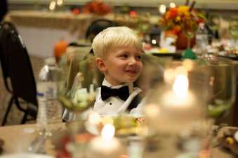 a young boy sitting at a wedding table smiling