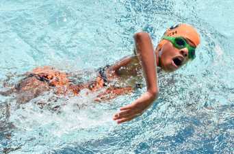 a kid in a swimming cap taking a breath during his swimming race