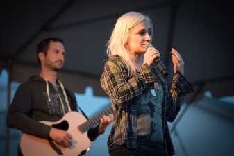 a woman singing while a man behind her plays guitar