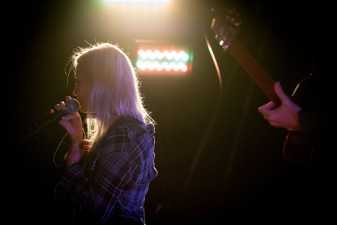 a woman singing on a dark stage beside a man with a guitar