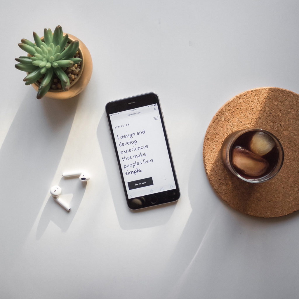 a succulent, ear buds, a phone, and drinking glass with ice
